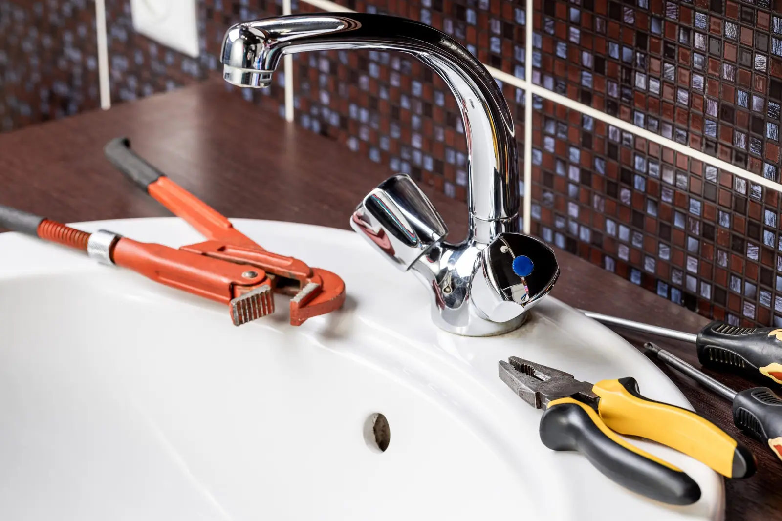 Chrome kitchen faucet with plumbing tools arranged on the sink
