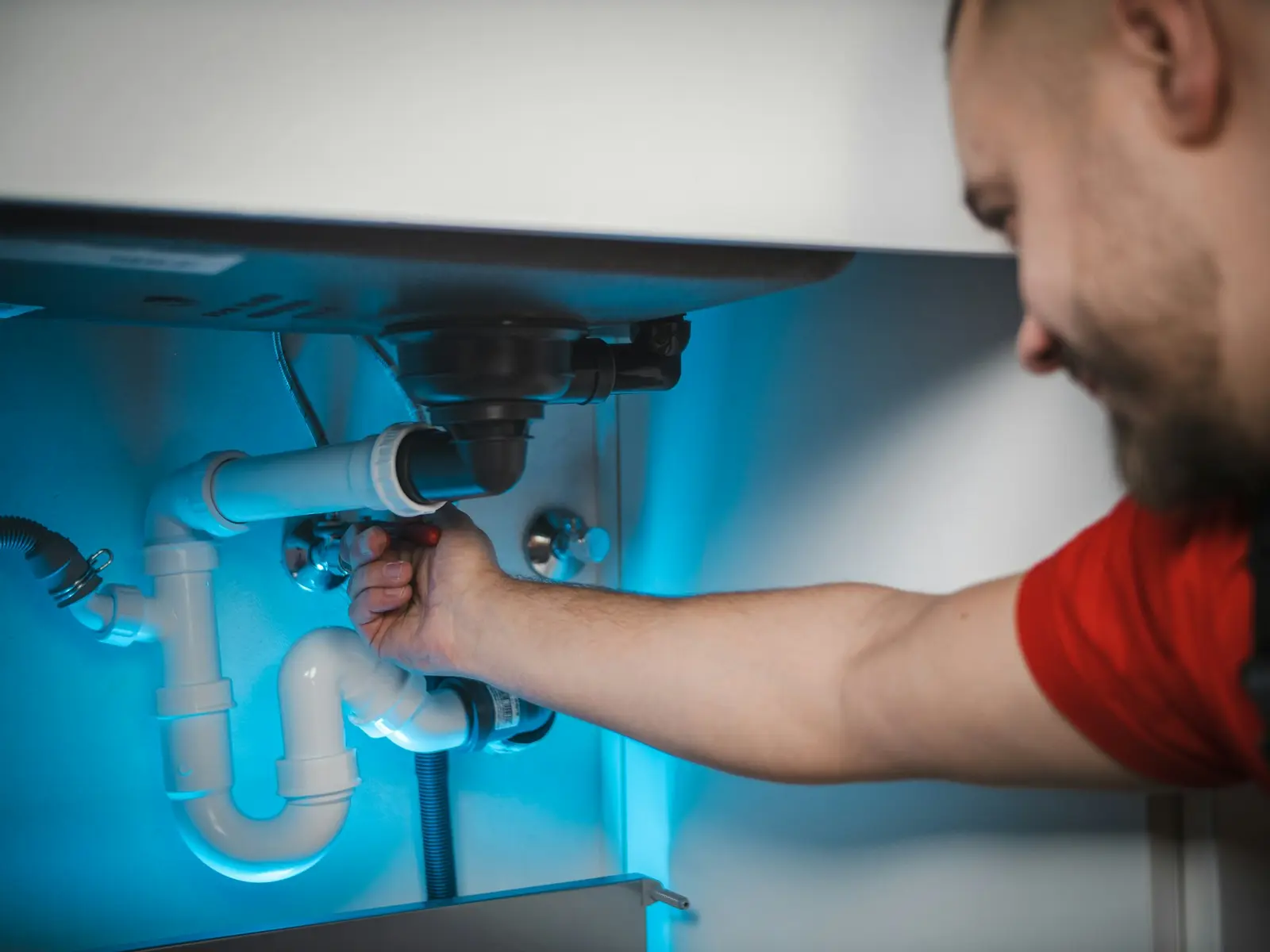 Plumber repairing the drain connections beneath a kitchen sink